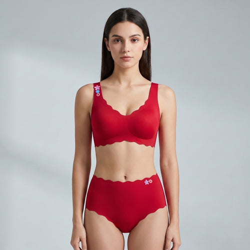 A woman modeling a matching red two-piece underwear set with scalloped edges, featuring a bra top and high-waisted briefs, against a light gray studio background.